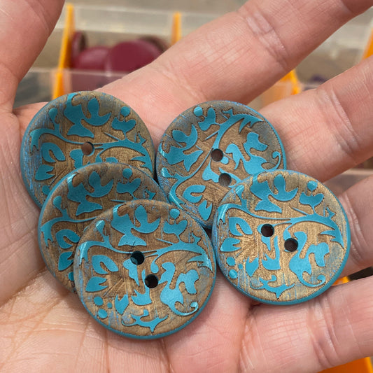 Hand holding four blue decorative buttons with floral patterns.