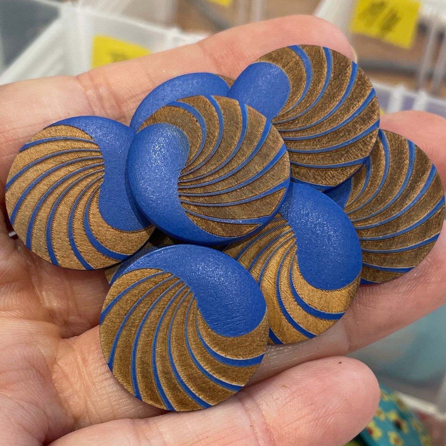 Hand holding blue and gold spiral buttons with a background of button containers.