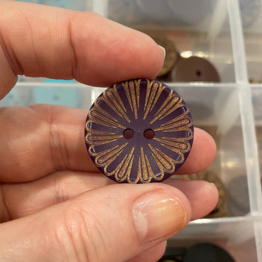 Hand holding a decorative button with a clear container of buttons in the background