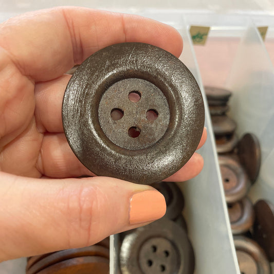 Hand holding a large metal button with a blurred background of more buttons.
