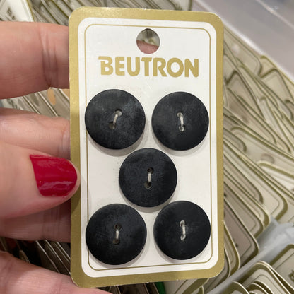 Hand holding a card with five black buttons labeled 'Beutron' amidst more cards in the background.