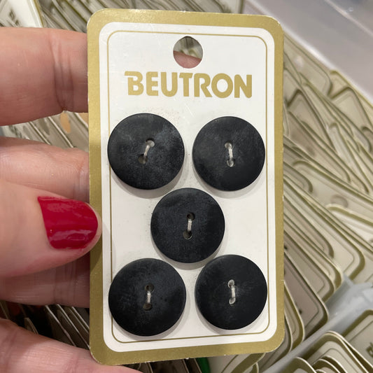 Hand holding a card with five black buttons labeled 'Beutron' amidst more cards in the background.