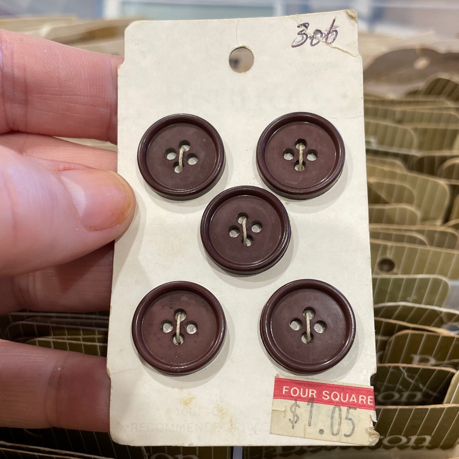 Card with six brown buttons held by a hand, with more cards in the background.