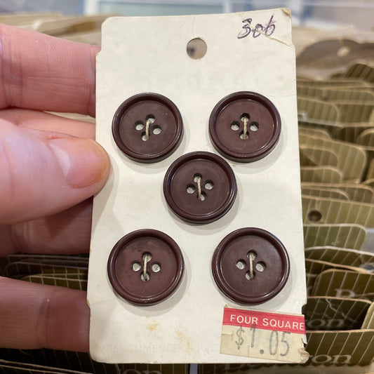 Card with six brown buttons held by a hand, with more cards in the background.
