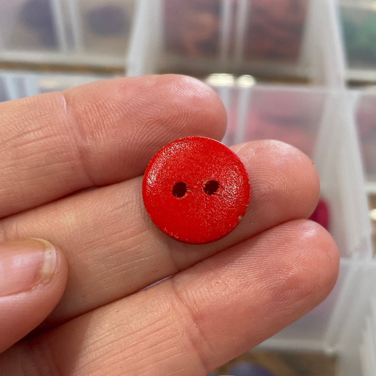 Hand holding a red button with a blurred background of a button organizer.