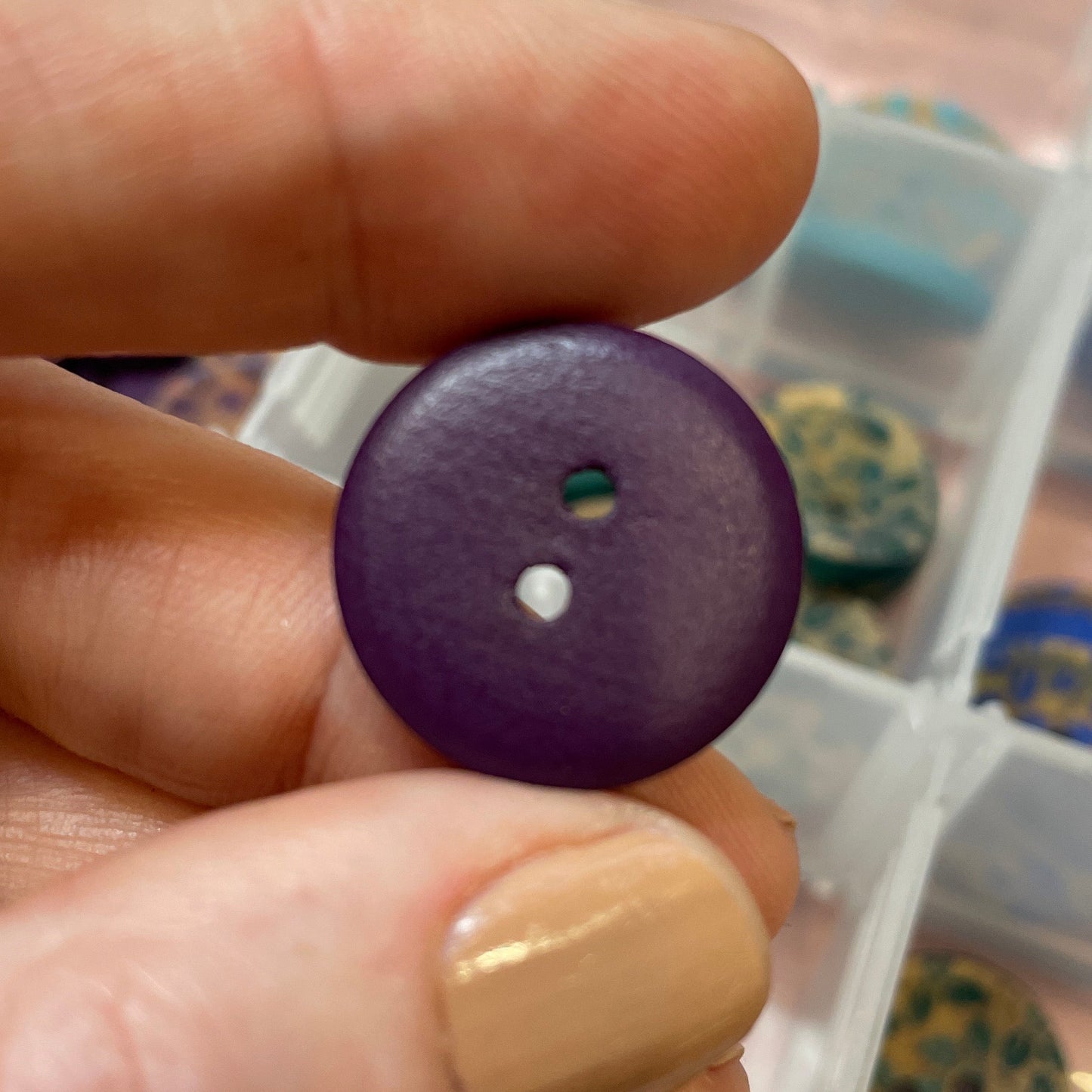 Hand holding a purple button with a container of buttons in the background