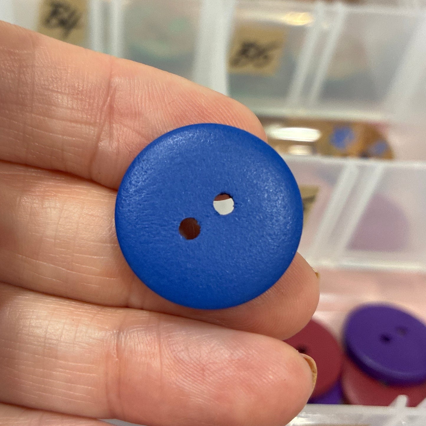 Blue button held between fingers with a blurred background of button collection