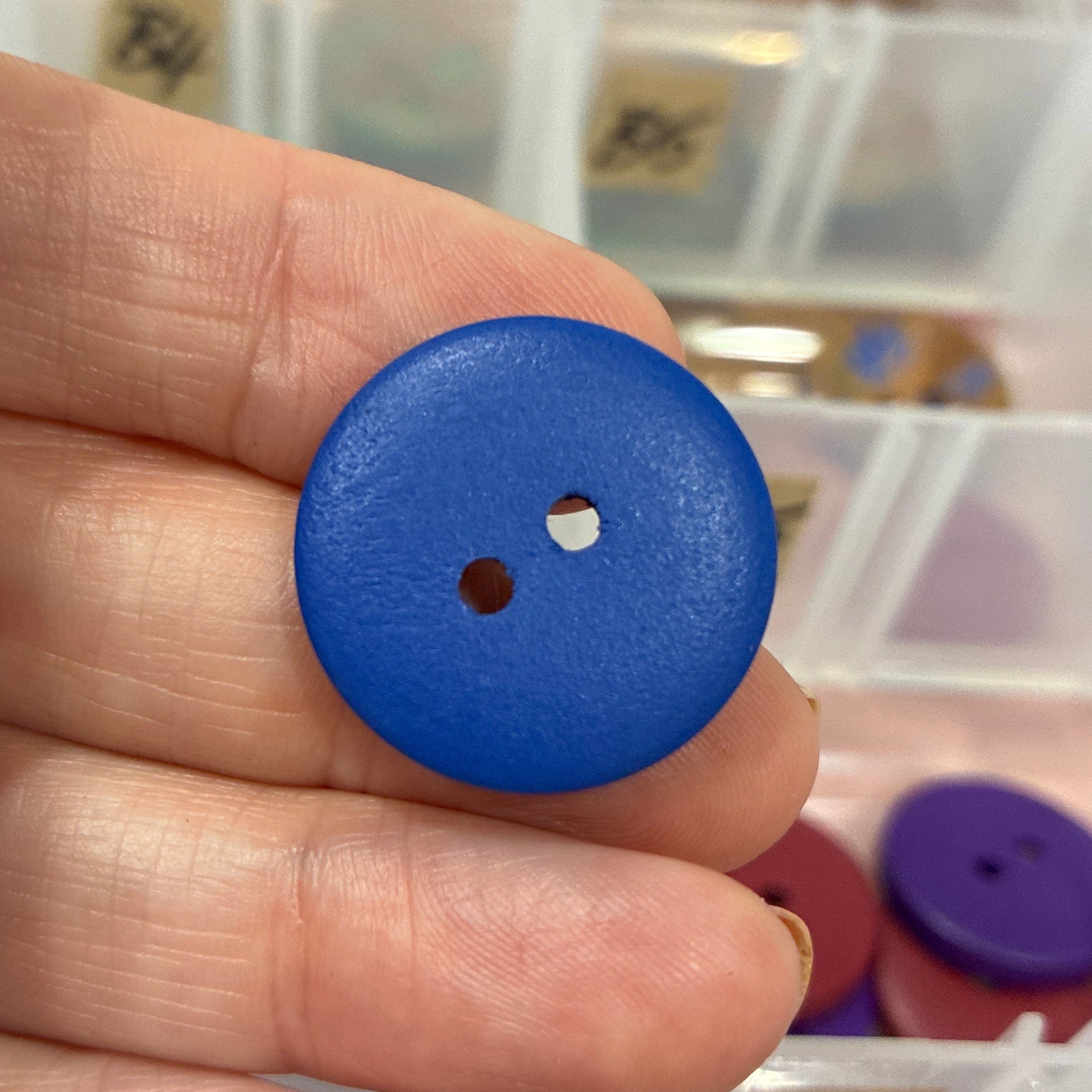 Blue button held between fingers with a blurred background of button collection