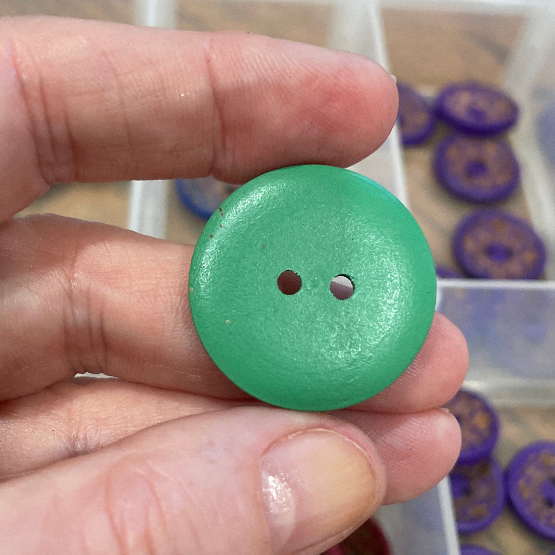 Green button held by a hand with a container of buttons in the background