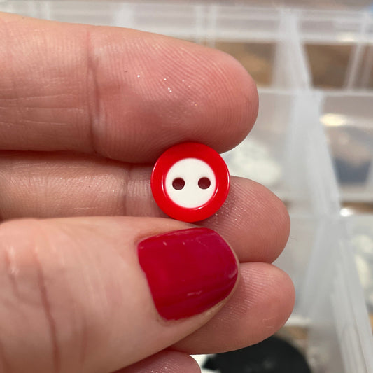 Red button held between fingers with a container of buttons in the background