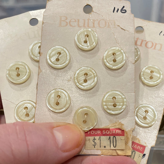 Hand holding a package of buttons with a clear plastic container in the background