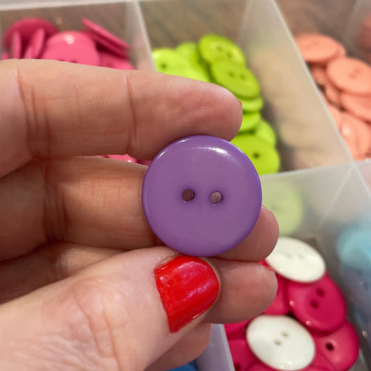 Hand holding a purple button with a background of colorful buttons in a container
