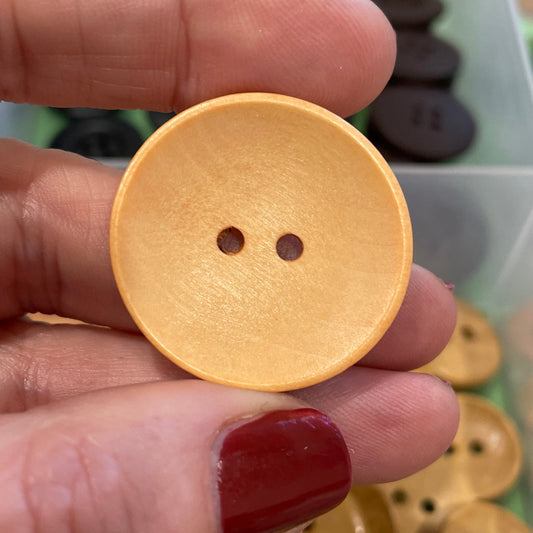 Gold button held by a hand with red nail polish, against a background of assorted buttons.