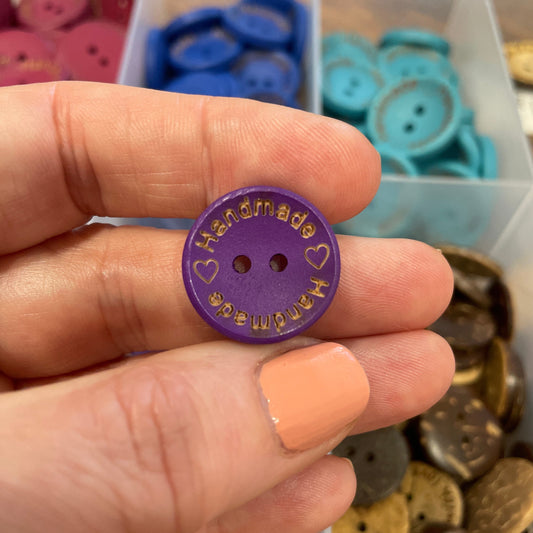 Hand holding a purple button with text against a background of assorted buttons.