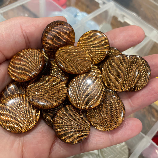 Hand holding gold metallic buttons with a background of a container with various buttons.