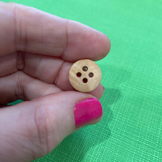 Wooden button held between fingers against a green background