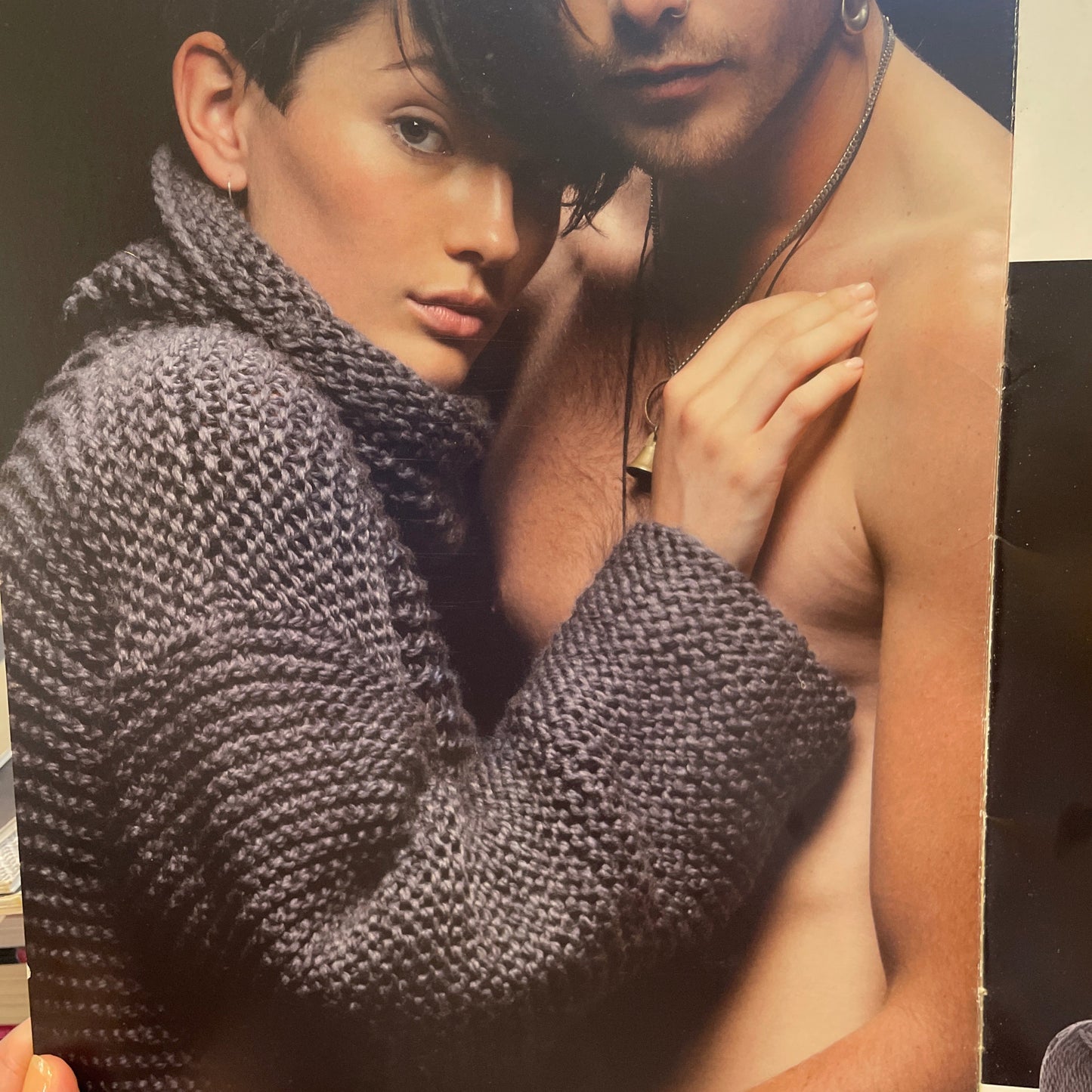 Person wearing a textured garment with another person holding them, on a black and white striped background.