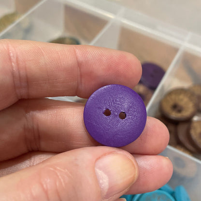 Hand holding a purple button with a container of buttons in the background