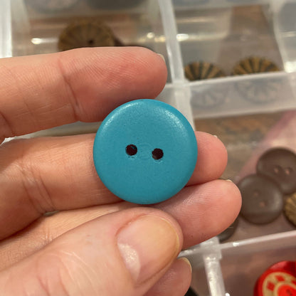 Hand holding a blue button with a container of assorted buttons in the background