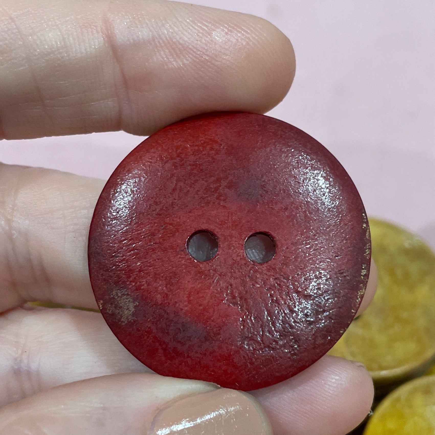 Hand holding a red button with other buttons in the background on a pink surface