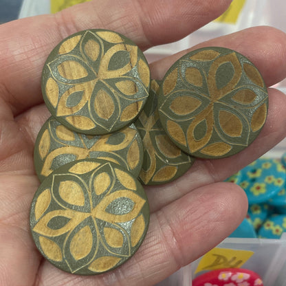 Hand holding green floral-patterned buttons with button collection in the background