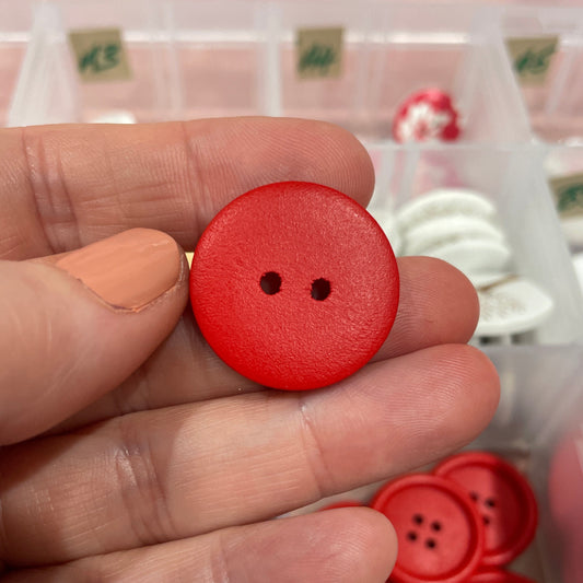 Hand holding a red button with a container of buttons in the background