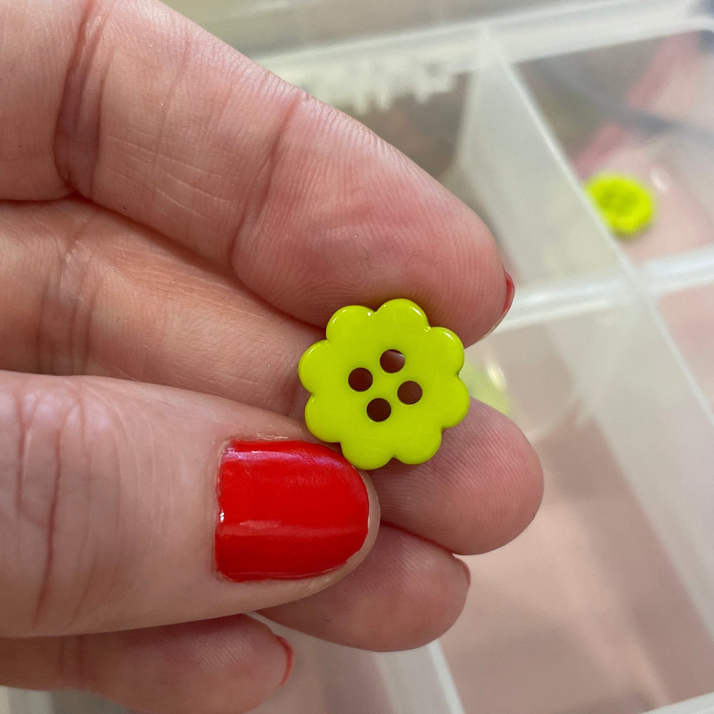 Hand holding a yellow flower-shaped button with a clear container of buttons in the background