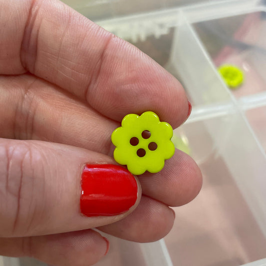 Hand holding a yellow flower-shaped button with a clear container of buttons in the background