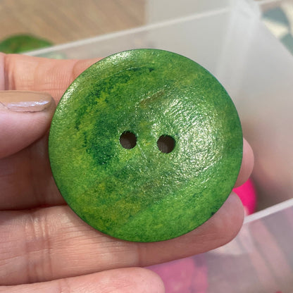 Green button held by a hand with pink buttons in the background
