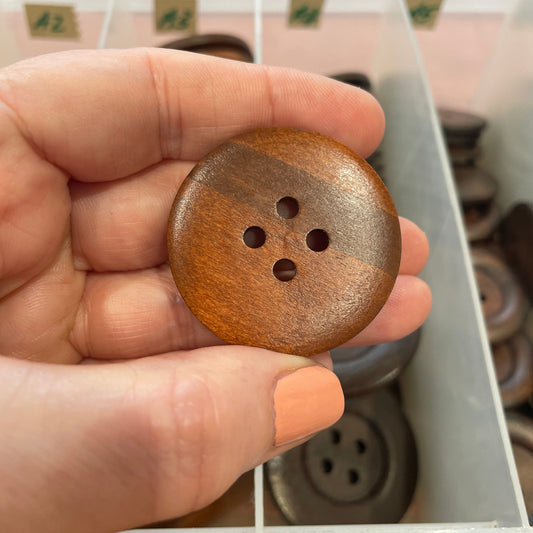 Hand holding a wooden button with a blurred background of shelves.