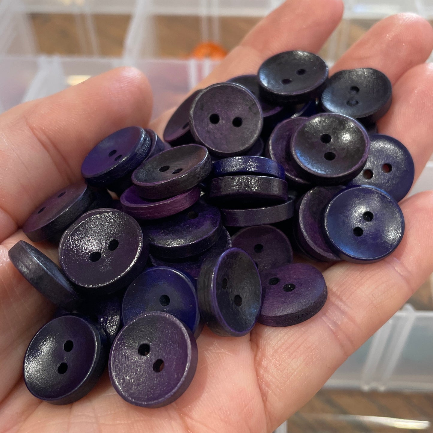 Hand holding purple buttons with a blurred background of button containers.