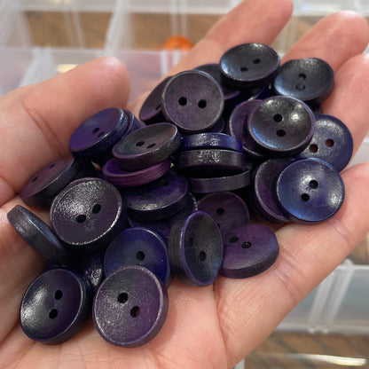 Hand holding purple buttons with a blurred background of button containers.