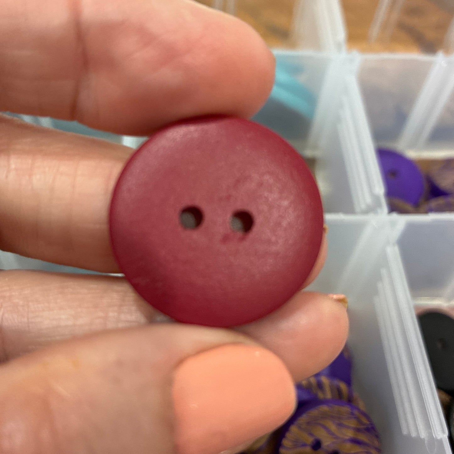 Hand holding a red button with a background of a storage box with various items.