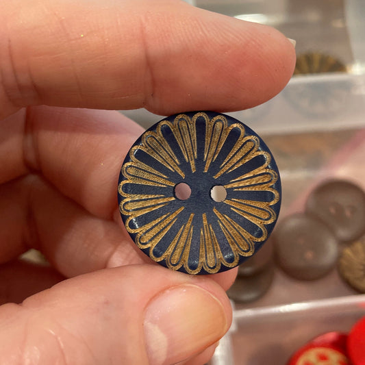 Hand holding a decorative button with a collection of buttons in the background.