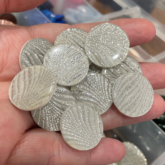 Hand holding silver circular objects with a blurred background of a storage box.