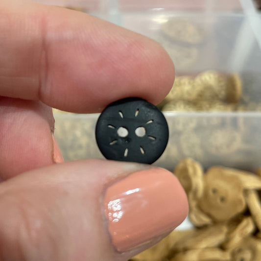 Hand holding a small black button with a blurred background of button collection