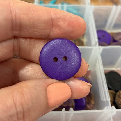 Purple button held between fingers with a container of buttons in the background