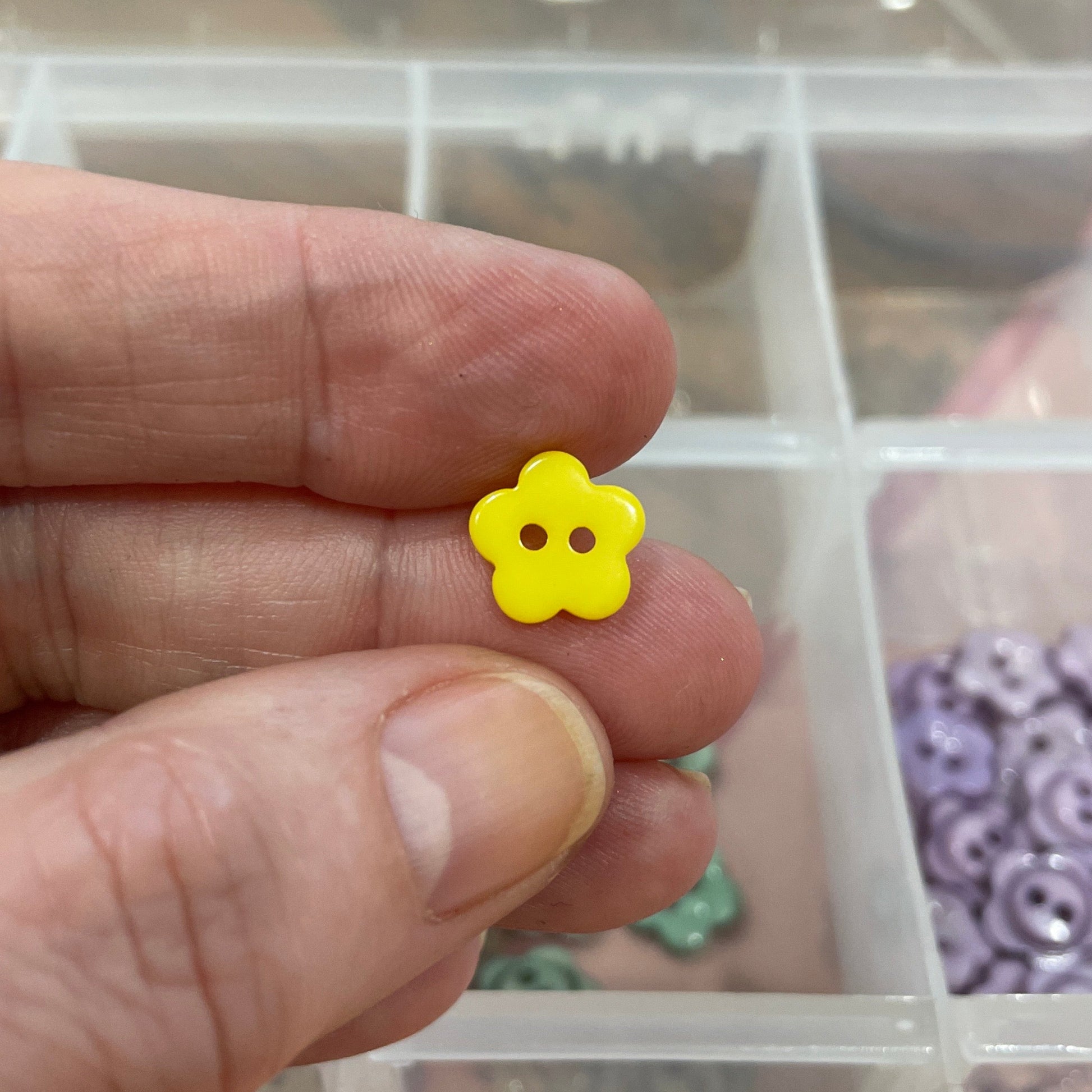 Hand holding a yellow flower-shaped object with a container of assorted small objects in the background.