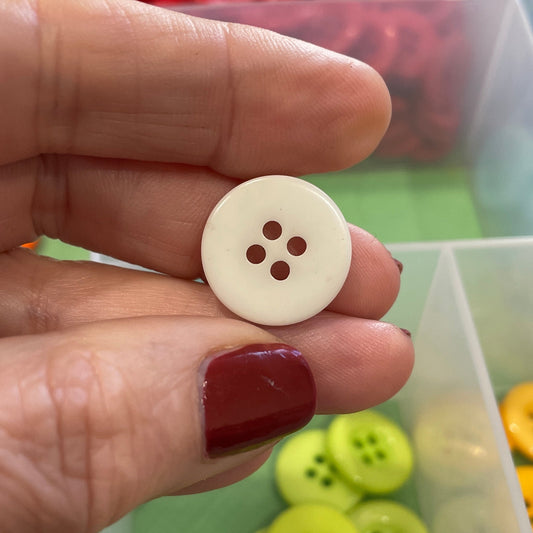 Hand holding a white button with a button organizer in the background