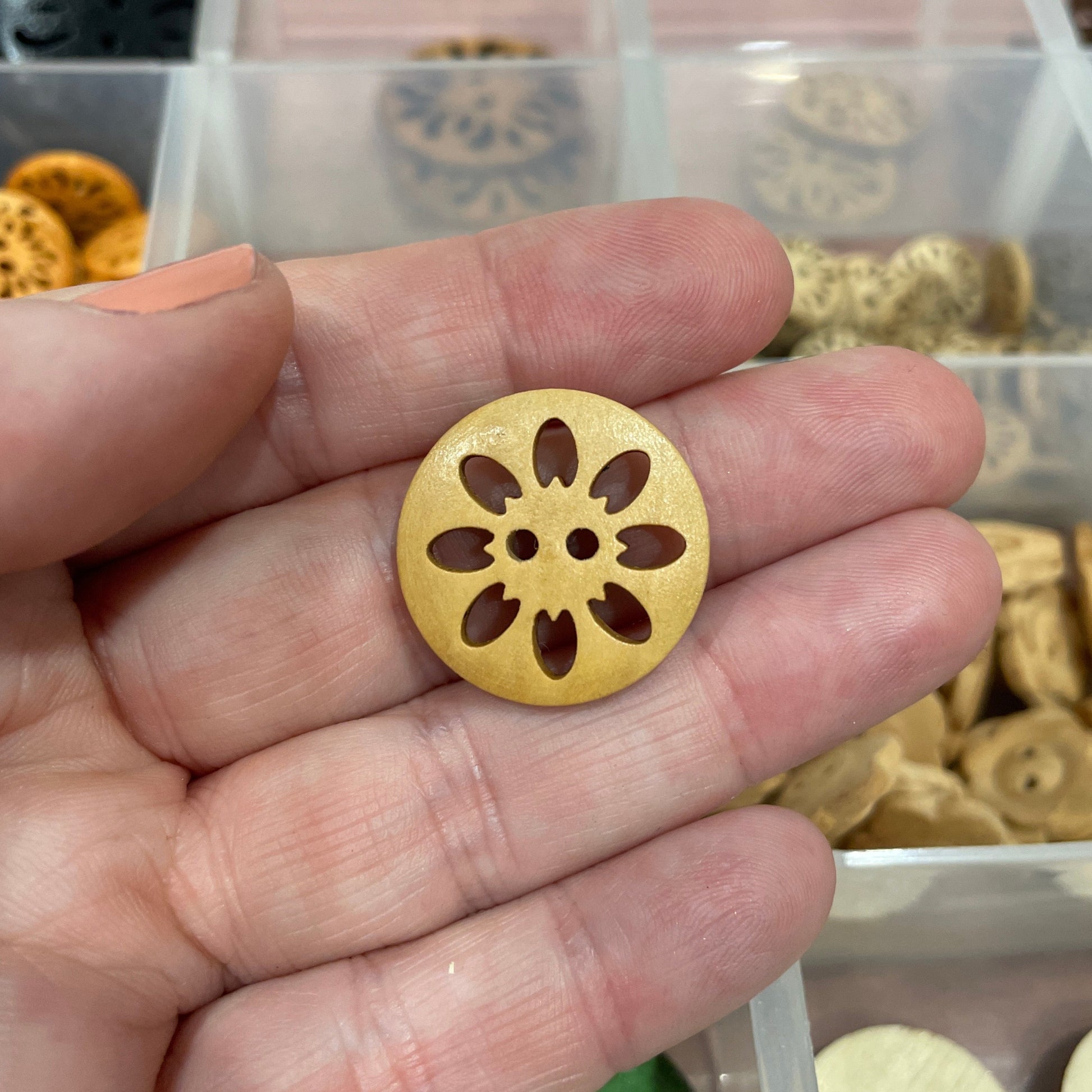 Gold decorative button held by a hand with a container of buttons in the background