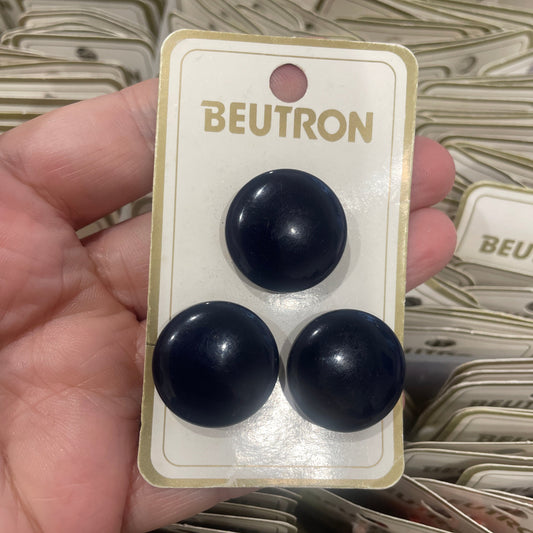 Three black buttons on a Beutron card held in a hand with a blurred background.