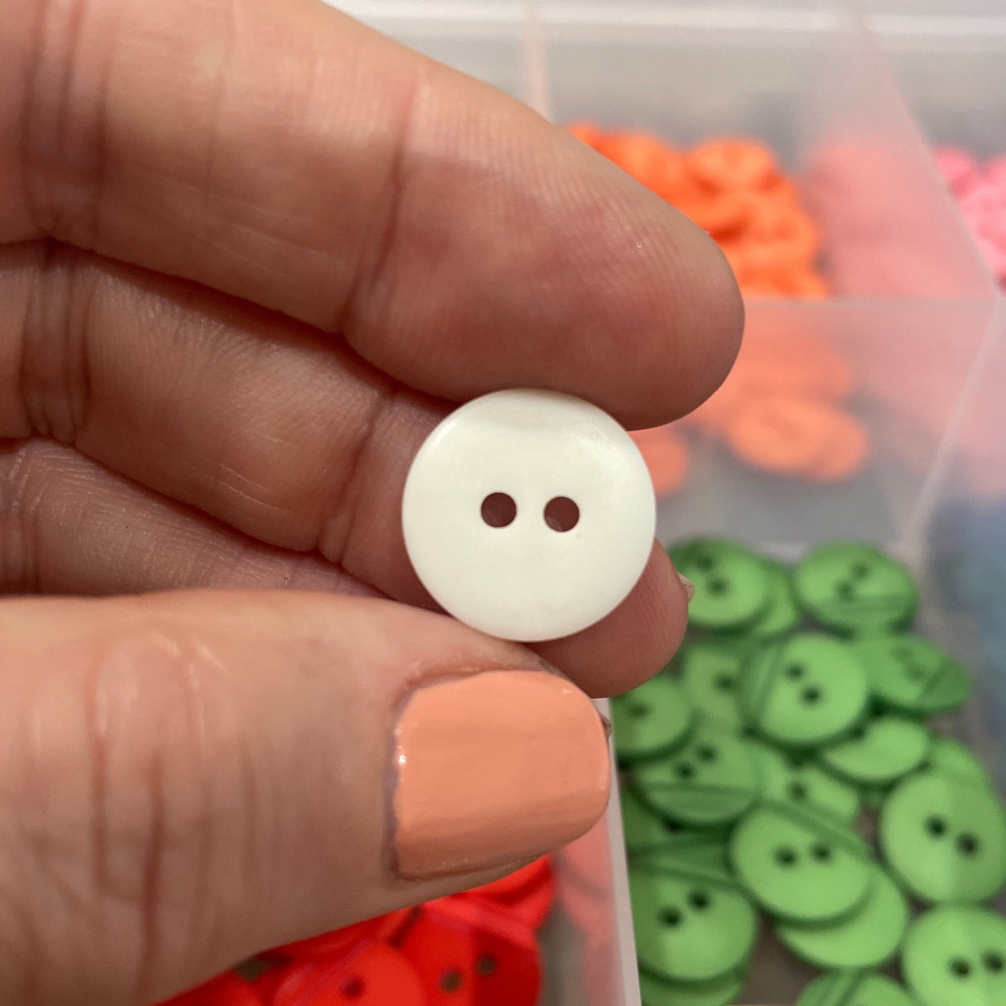 Hand holding a white button with a container of colorful buttons in the background