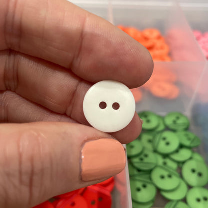Hand holding a white button with a container of colorful buttons in the background