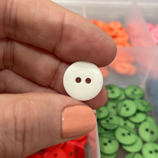 Hand holding a white button with a container of colorful buttons in the background