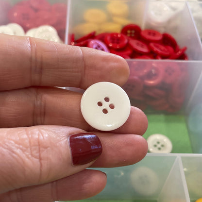 Hand holding a white button with a background of colorful buttons in a box