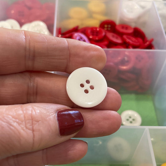 Hand holding a white button with a background of colorful buttons in a box