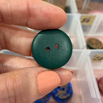 Green button held between fingers with a background of small containers.