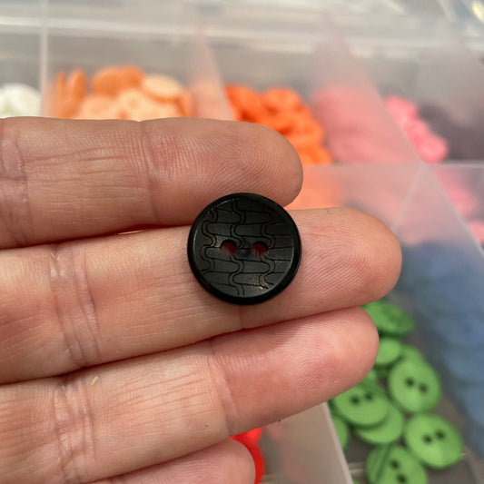 Black button held between fingers with a container of colorful buttons in the background