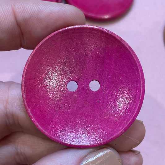 Hand holding a pink button with other colorful buttons in the background