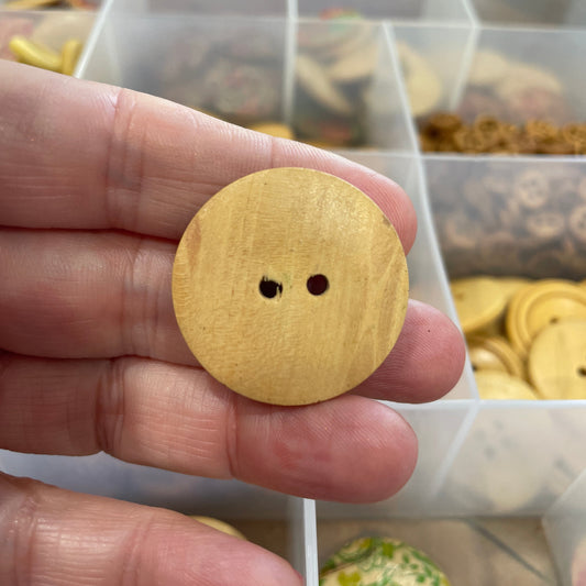 Wooden button held between fingers with a blurred background of similar buttons.
